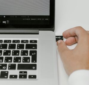 a hand putting a USB stick into the side of a laptop, providing a back up in the event of a cyber attack